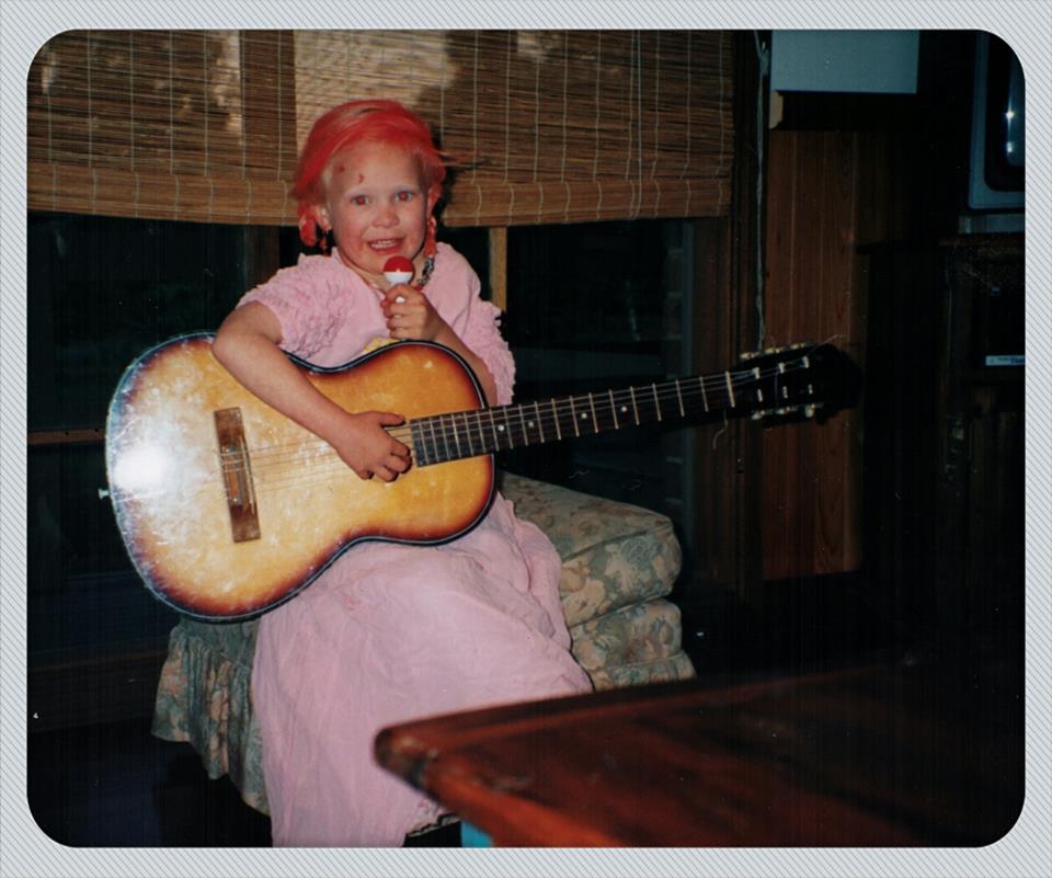 A photo that my mother took of me when I was 5 years old with red spray-painted hair, a 1980s puffy pink dress and a nylon strong guitar. 